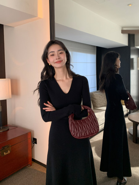 Woman wearing a long black dress and holding a burgundy handbag in a mirror selfie