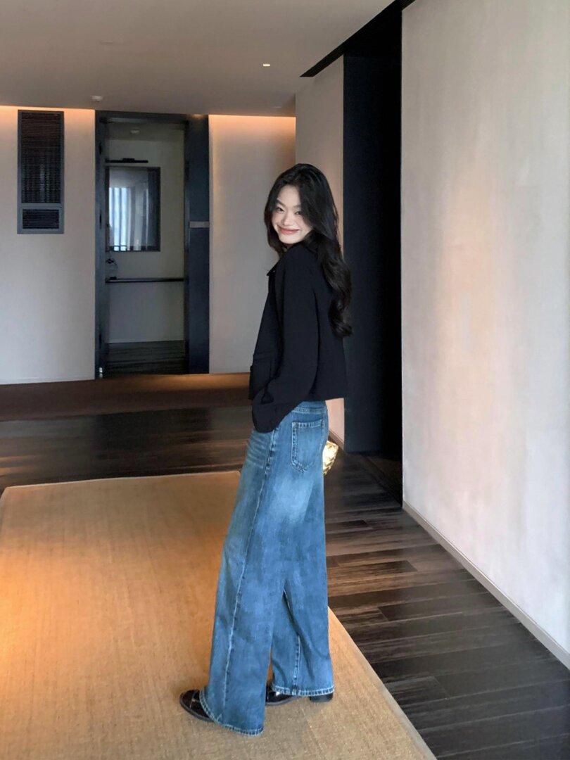 Woman modeling wide-leg blue jeans with a black top indoors