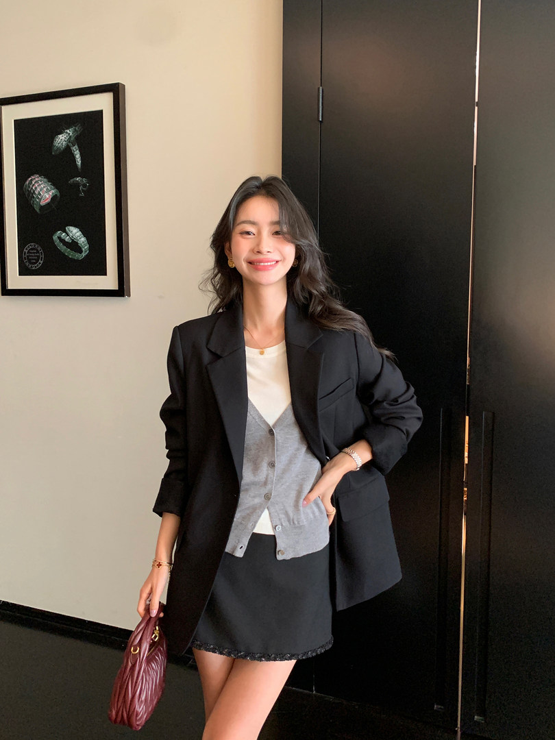 Woman wearing a black blazer over a layered gray-and-white outfit with a mini skirt