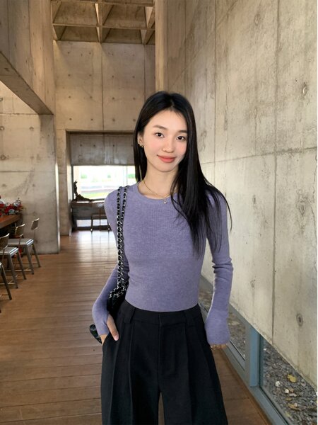 Woman wearing a lilac long-sleeve knit top with black pleated pants and a chain-strap bag