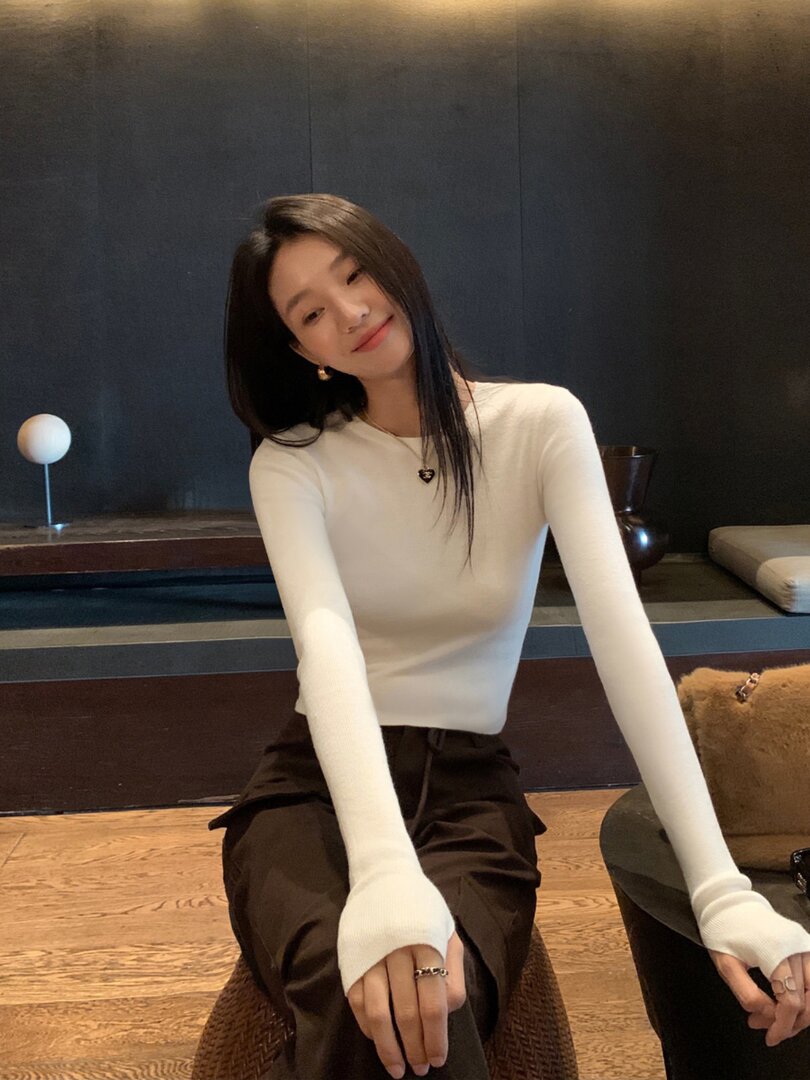 Woman wearing a white fitted long-sleeve top with dark pants indoors