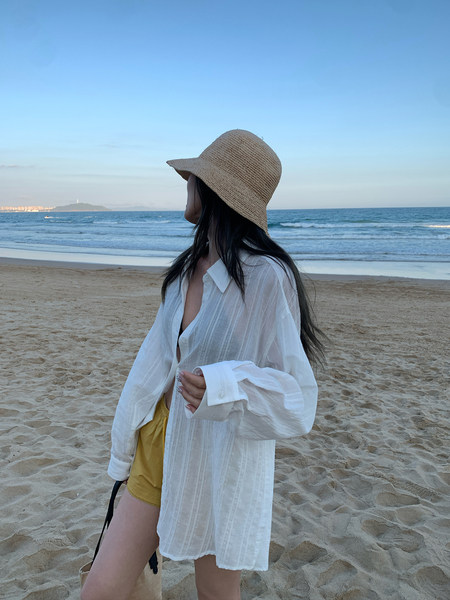 Woman wearing a sheer white oversized shirt and straw hat on a beach