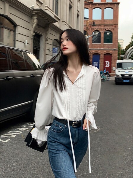 Woman wearing a white long-sleeve blouse with blue jeans on a city street