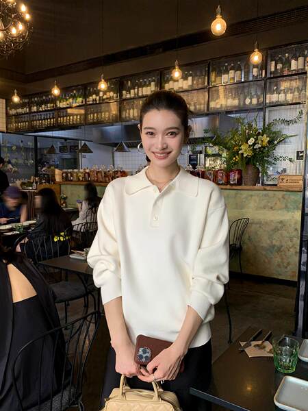 Woman wearing an off-white long-sleeve collared sweater and holding a beige handbag