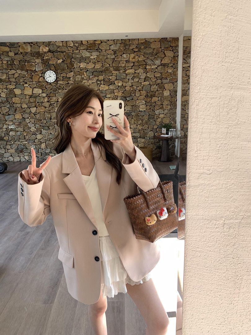 Woman wearing a beige oversized blazer with a white outfit in a mirror selfie