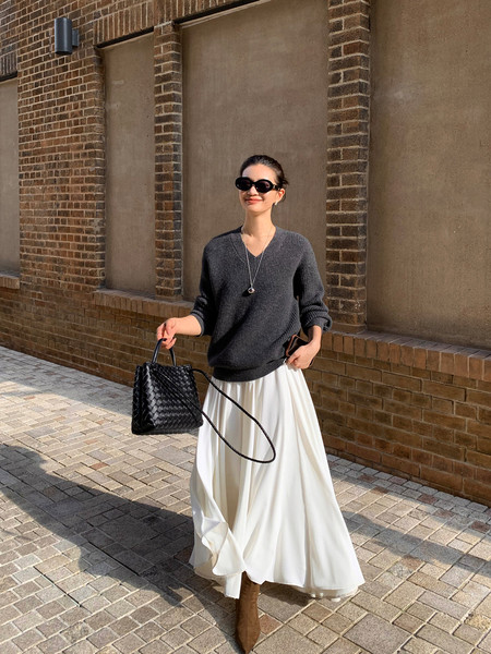 Woman modeling a dark sweater with a white flowy skirt and black handbag outdoors