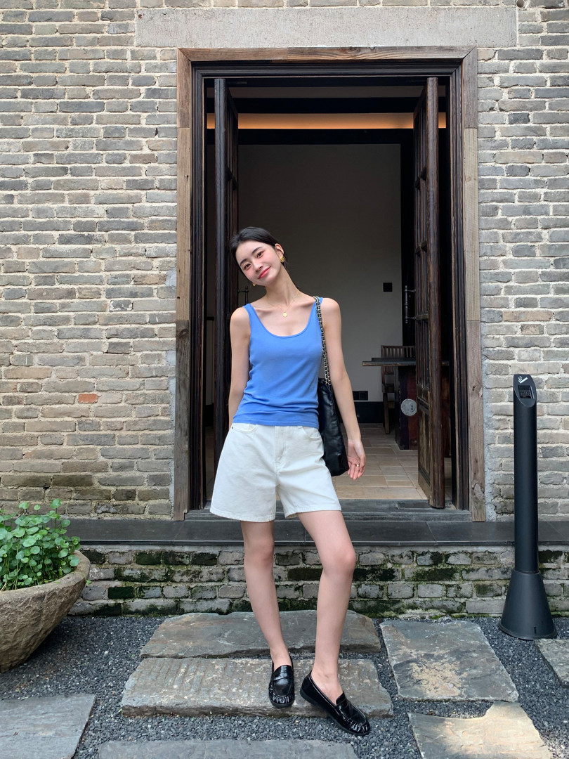 Woman wearing a blue tank top with white shorts and black loafers outdoors