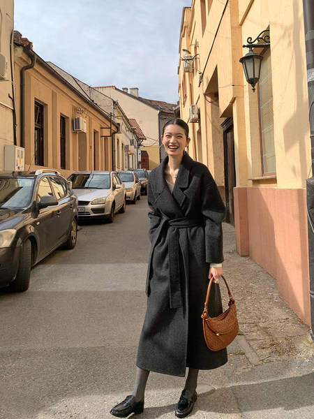 Woman wearing a dark belted long coat with a brown handbag on a city street