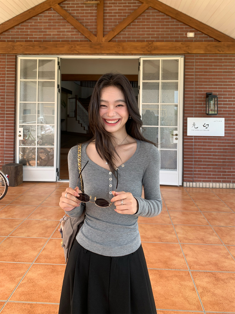 Smiling woman wearing a gray fitted long-sleeve top with a black skirt outdoors