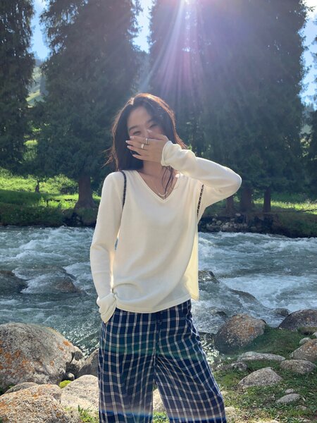 Woman wearing a white long-sleeve top and blue plaid pants outdoors by a river