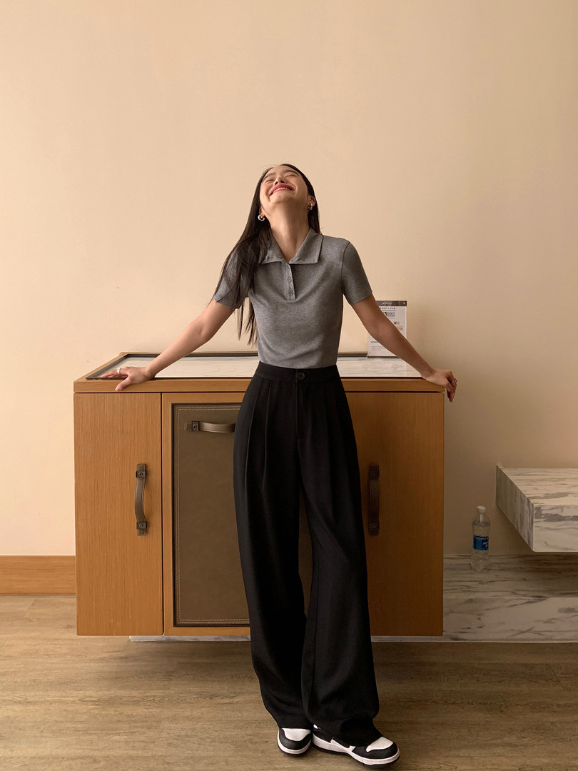 Woman wearing a gray polo top and black wide-leg pants indoors