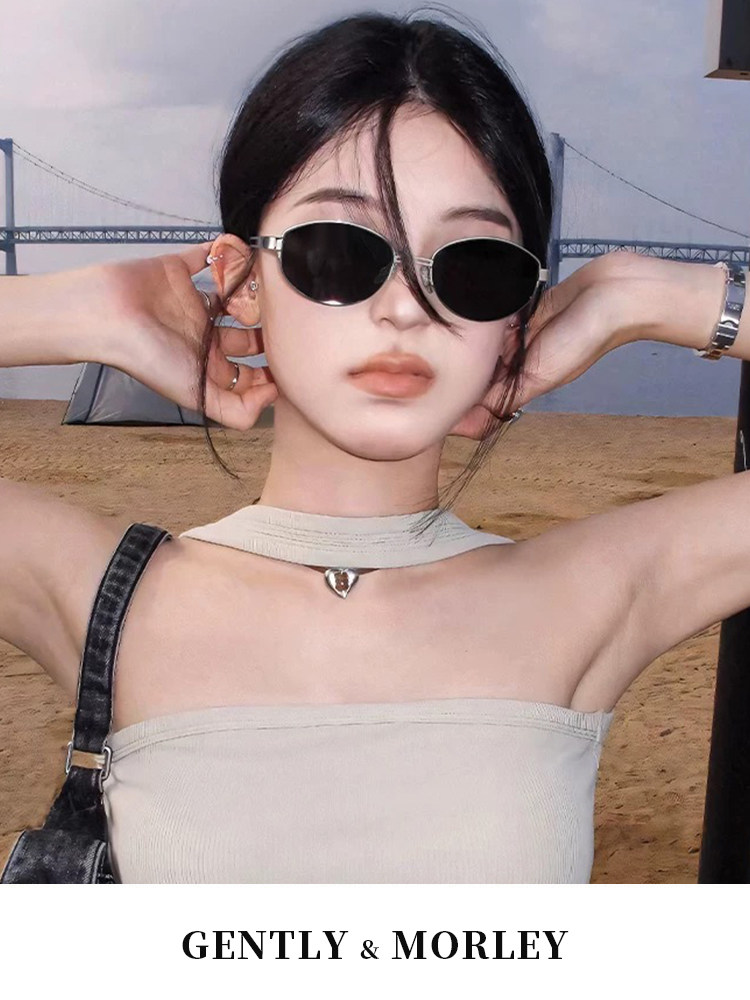 Model wearing black oval sunglasses with a beach backdrop