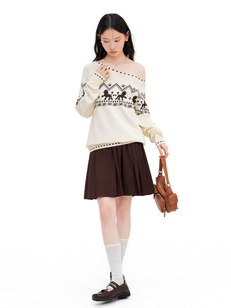 Model wearing a cream patterned off-shoulder sweater with a brown pleated skirt and small brown shoulder bag