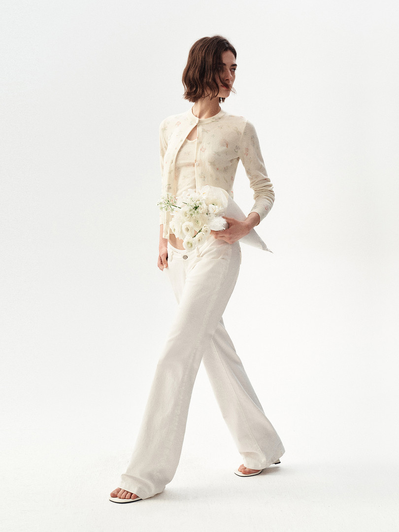 Model wearing an ivory cardigan, top, and wide-leg pants with a white floral bouquet