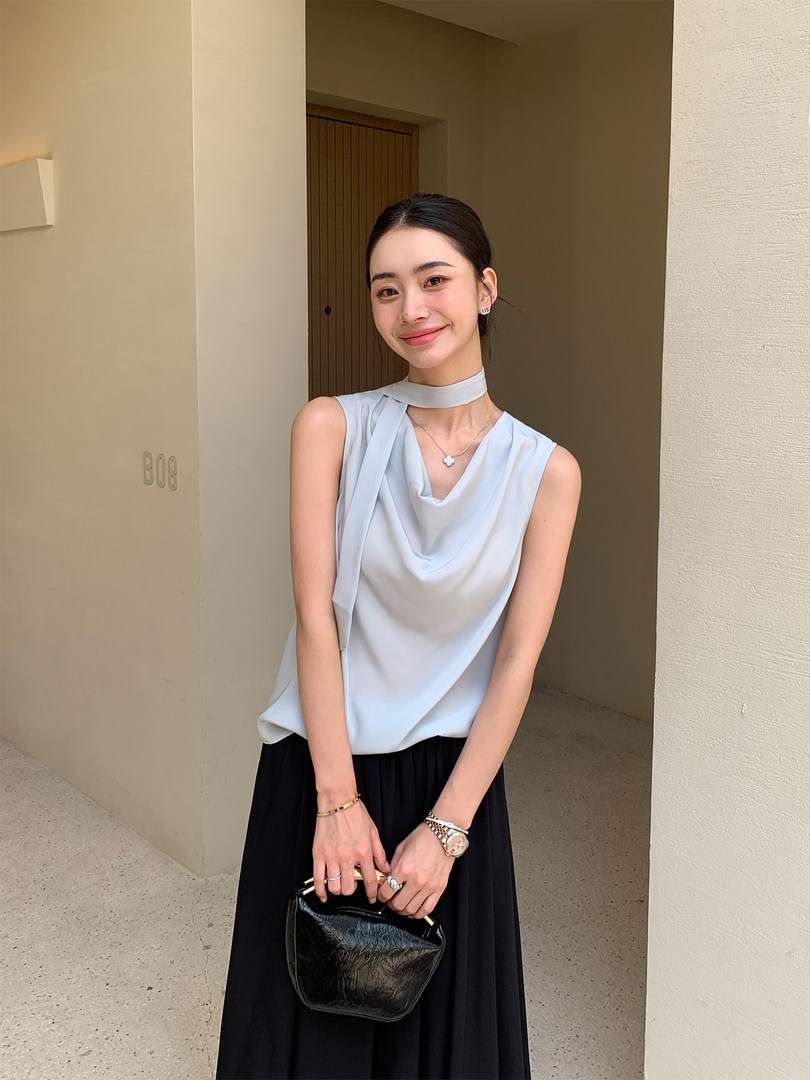 Woman modeling a light blue sleeveless draped top with a black skirt and black handbag