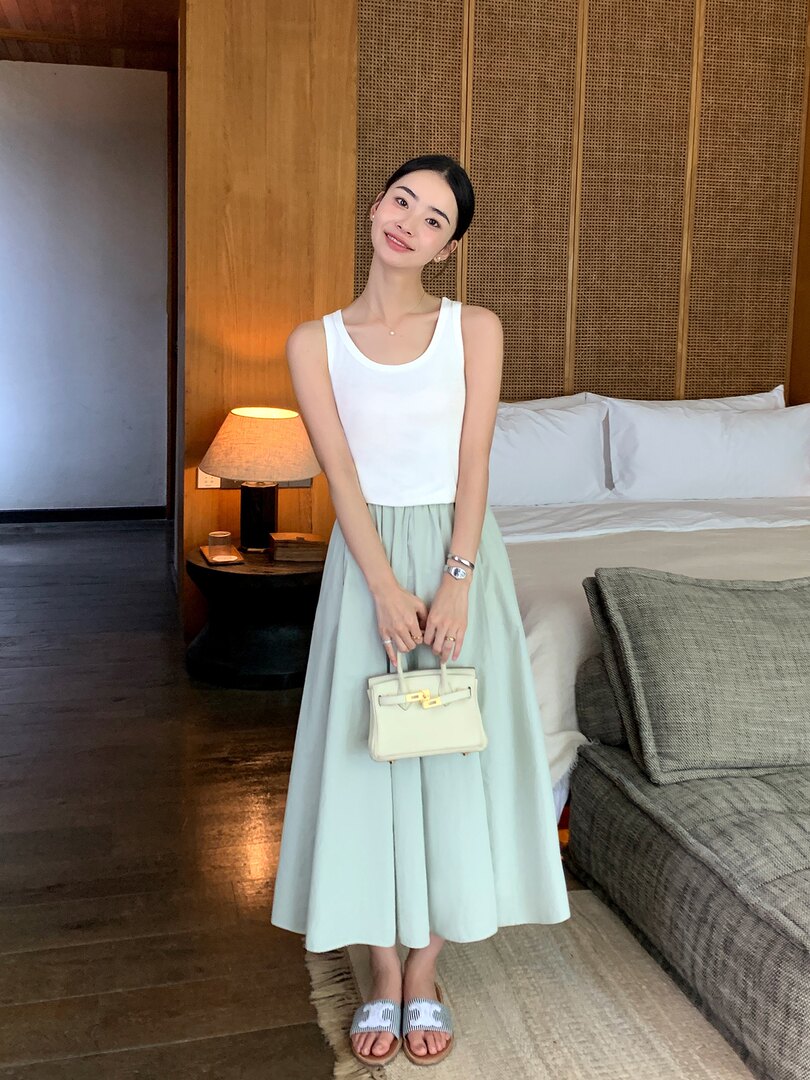 Model wearing a white sleeveless top with a light mint midi skirt, sandals, and a small handbag