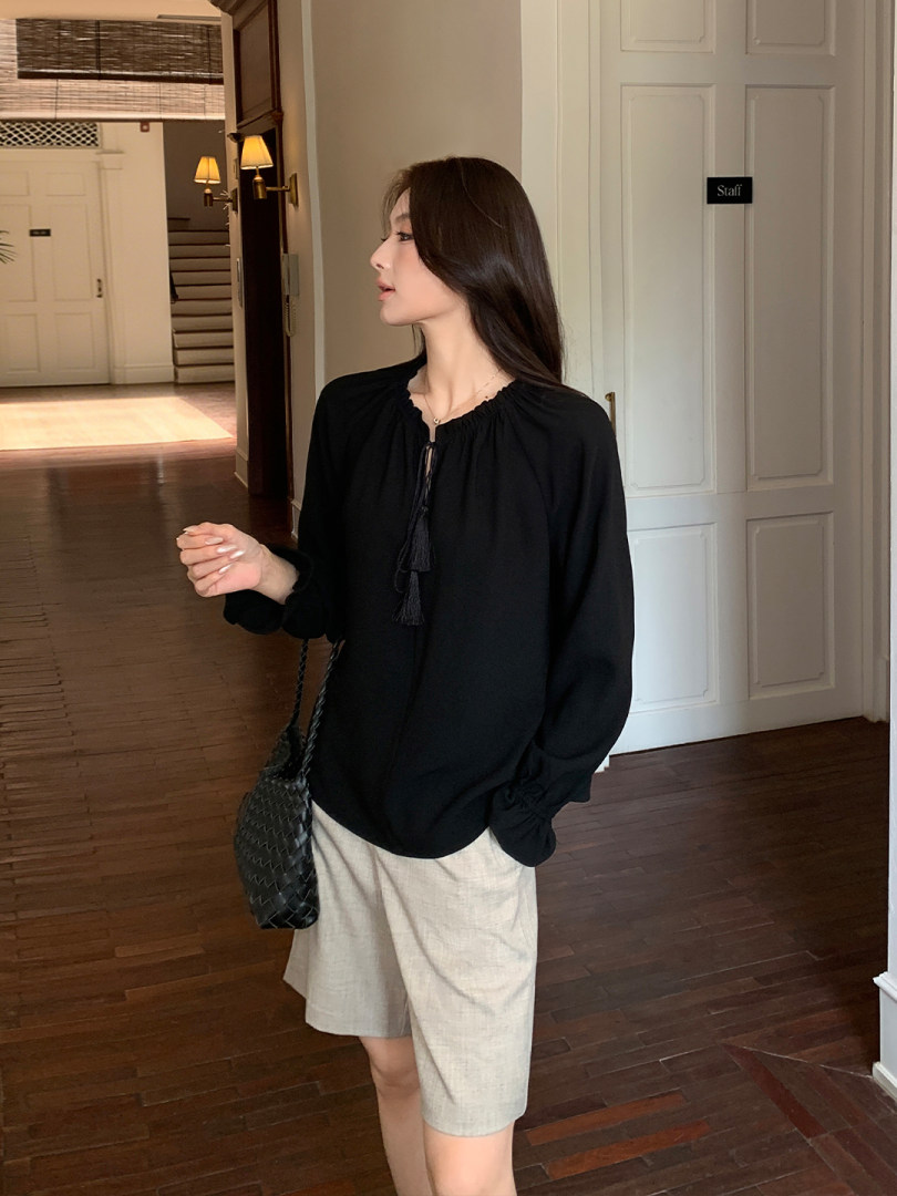 Black long-sleeve blouse worn with beige shorts on a model