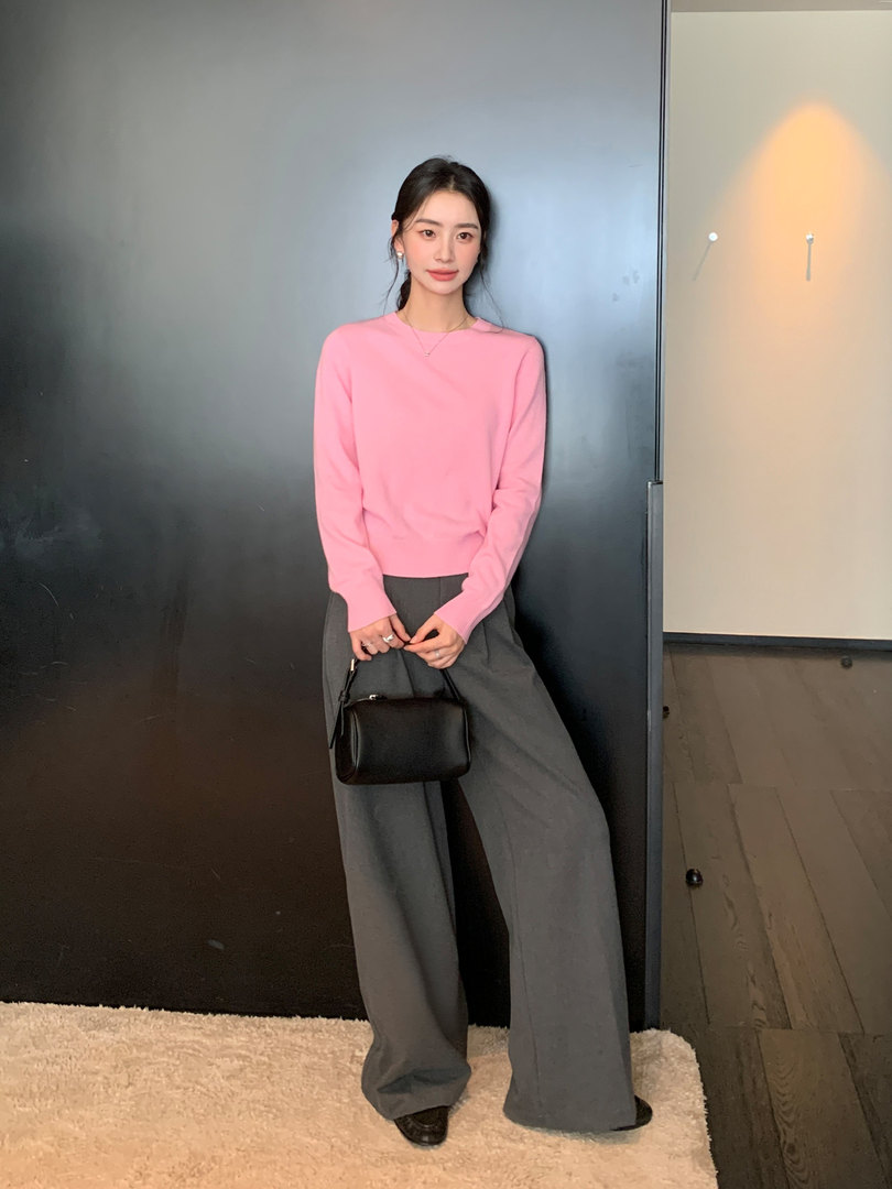 Woman wearing a pink long-sleeve top with wide gray pants and a black handbag