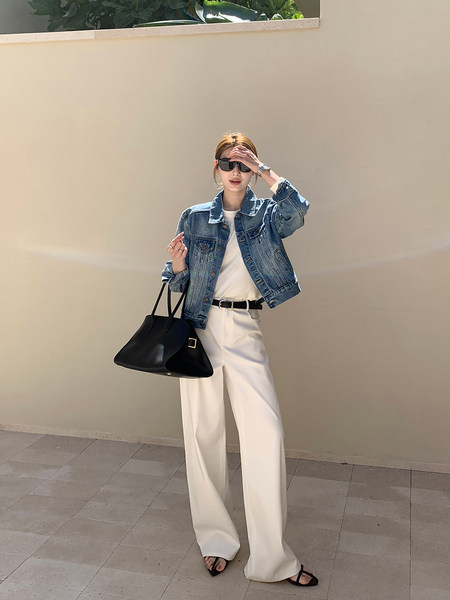 Woman wearing a denim jacket with white wide-leg pants and a black handbag