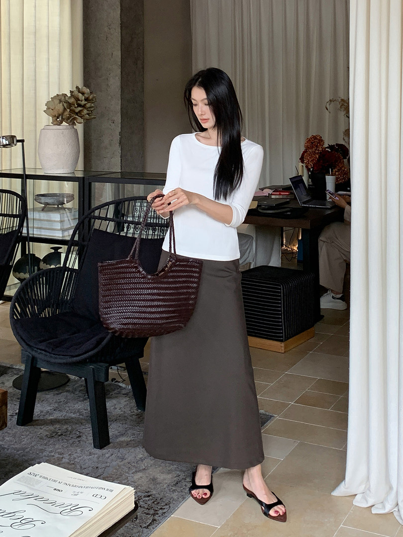 Woman wearing a white top with a brown maxi skirt and woven tote bag