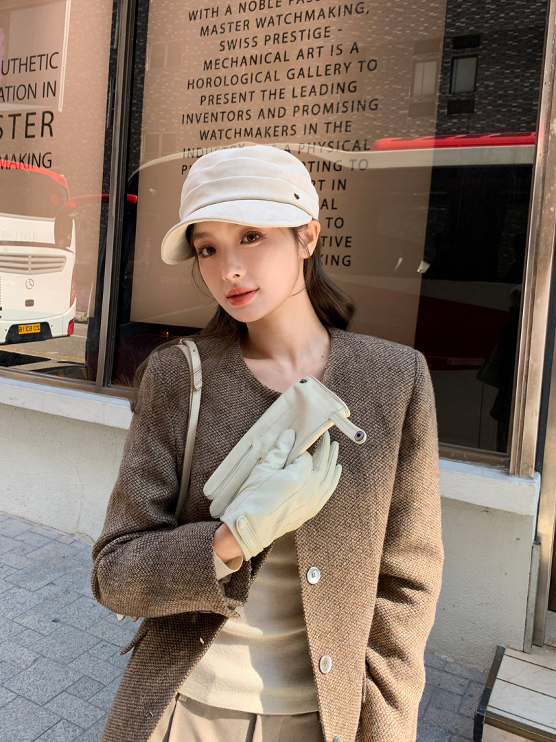 Woman wearing a brown textured coat with cream gloves and a white cap