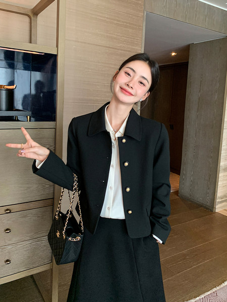 Woman wearing a black tailored suit with a white shirt and chain handbag