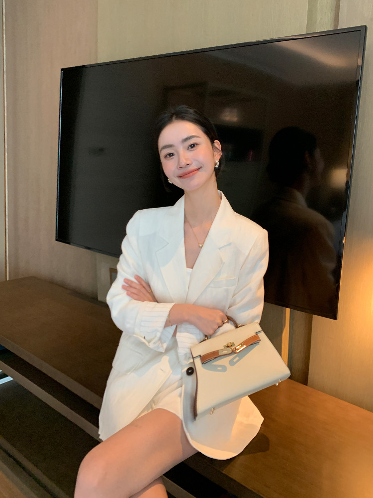 Woman wearing a white blazer and holding a cream handbag indoors