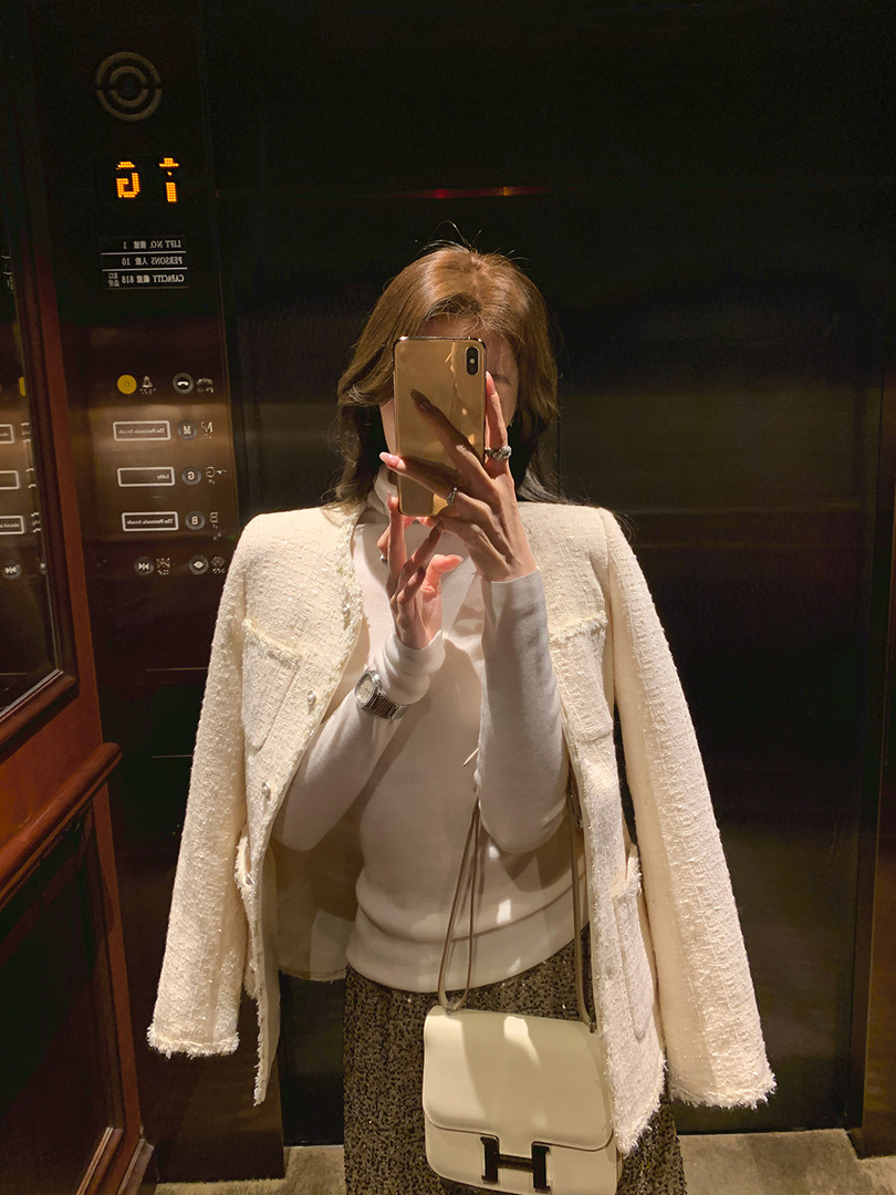 Woman taking a mirror selfie wearing a white textured jacket and carrying a cream crossbody bag
