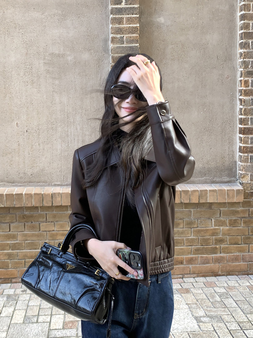 Woman wearing a dark brown leather jacket and holding a black handbag