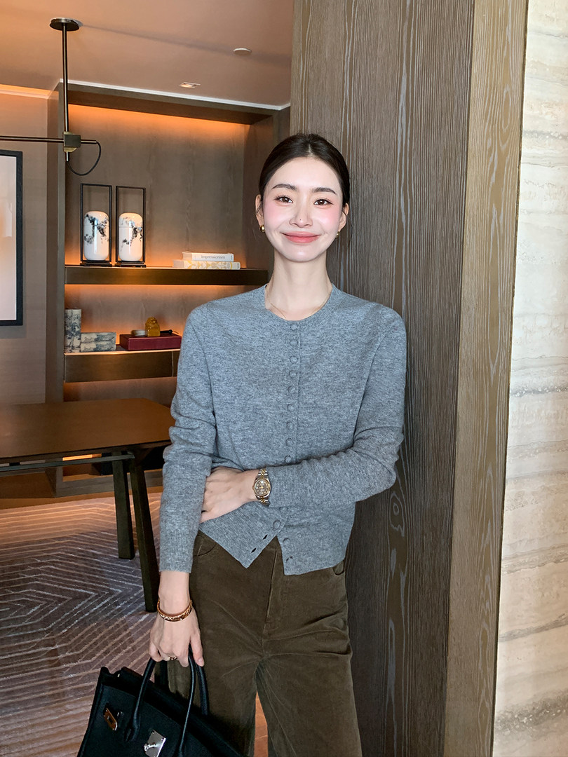 Woman wearing a gray button-front cardigan with brown trousers indoors