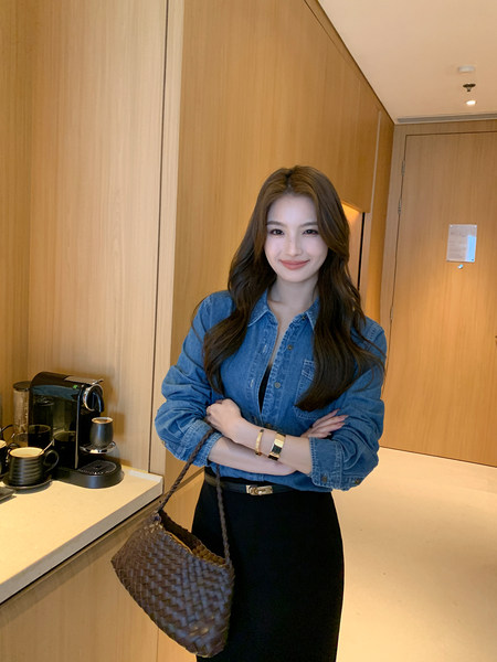 Woman wearing a blue denim shirt and black skirt with a woven tote bag