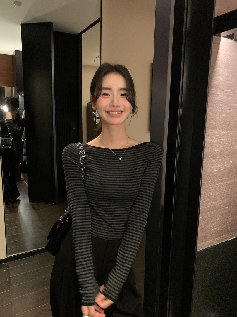 Woman wearing a black and gray striped long-sleeve top with a black skirt and shoulder bag