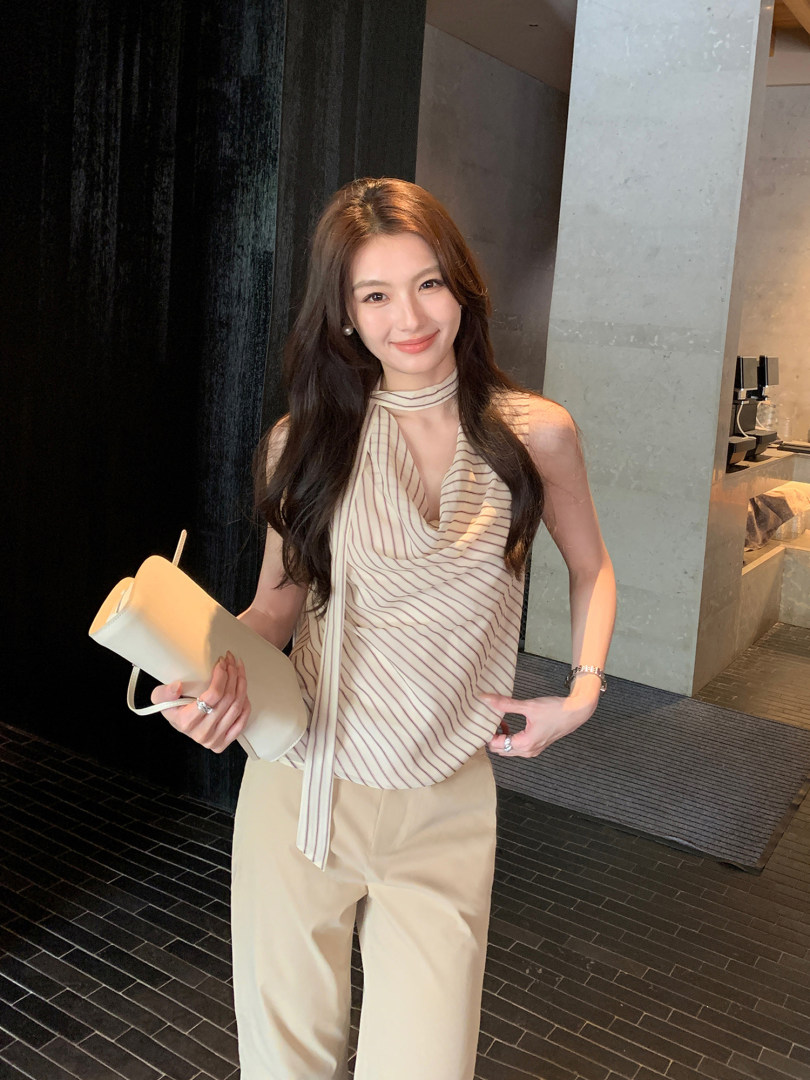 Woman wearing a striped halter top with beige trousers and holding a light-colored handbag