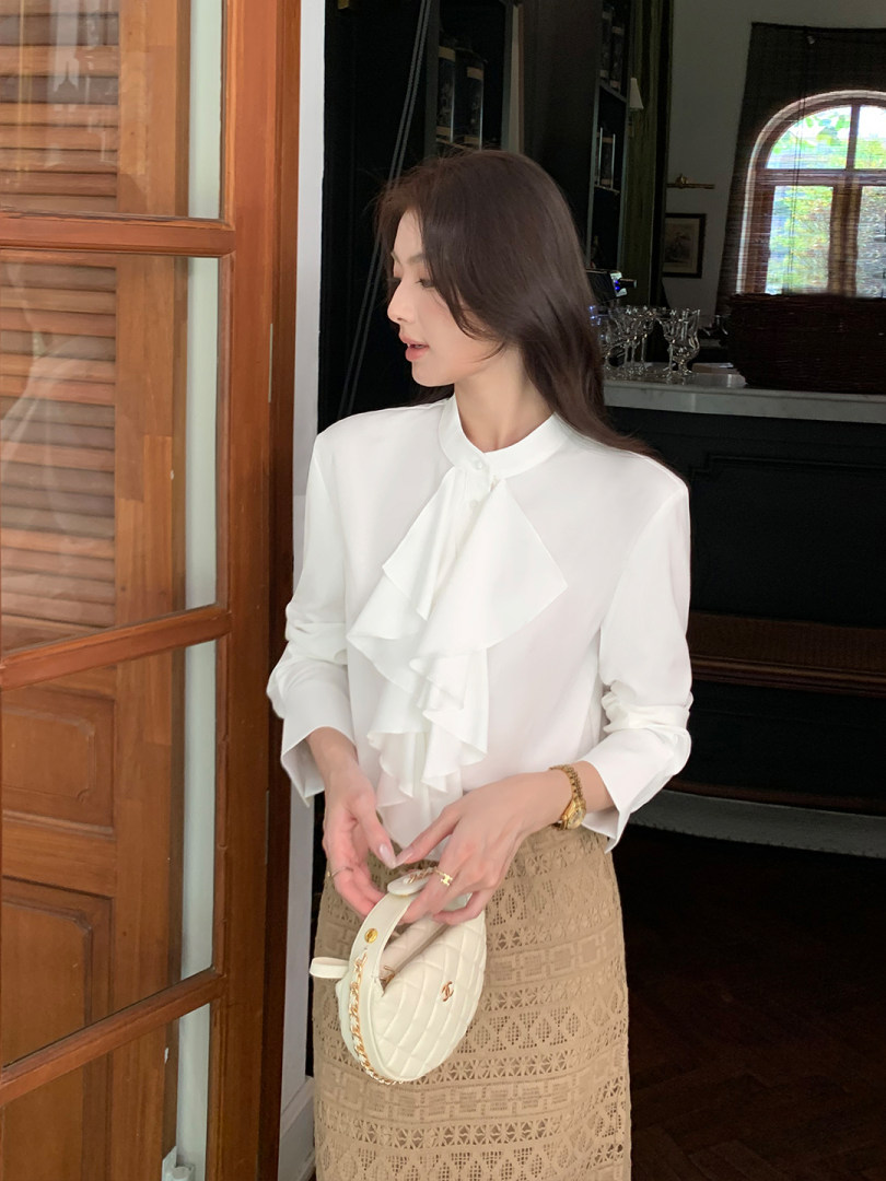 Woman wearing a white ruffled blouse and beige lace skirt while holding a white quilted handbag