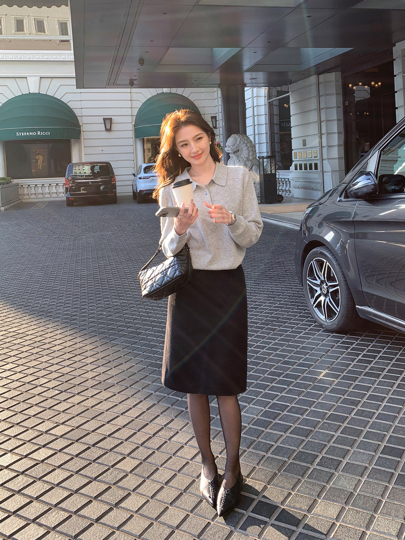 Woman wearing a grey knit top, black skirt, tights, and a quilted black handbag