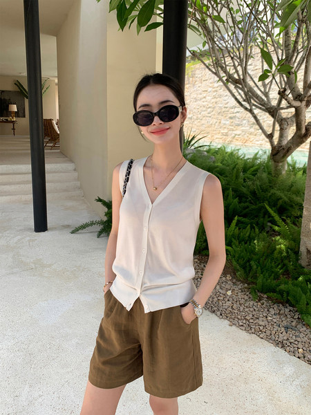 Woman wearing a sleeveless white button-front top with brown shorts outdoors