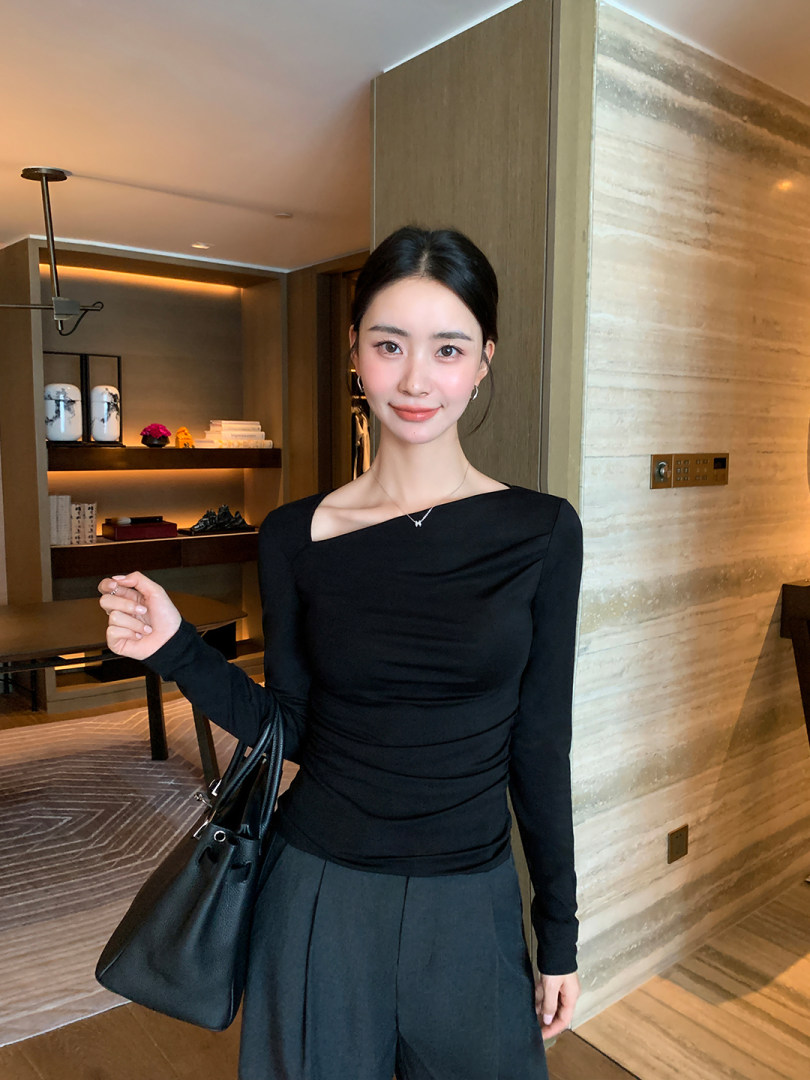 Woman wearing a black long-sleeve fitted top with dark trousers and carrying a black handbag