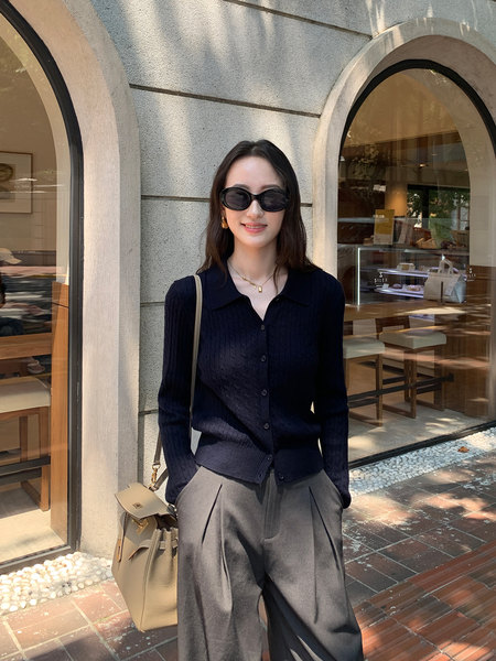 Woman wearing a navy cardigan with gray trousers and a beige handbag