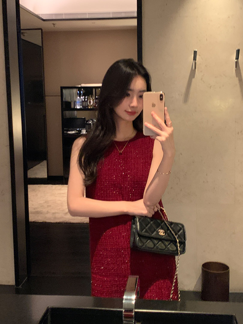 Woman wearing a red sleeveless dress holding a black quilted handbag in a mirror selfie