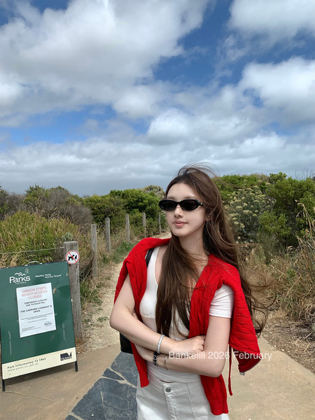 Woman wearing a white top, light pants, red sweater, and black sunglasses outdoors