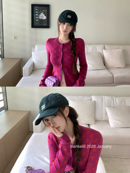 Model wearing a magenta patterned cardigan with a dark cap indoors