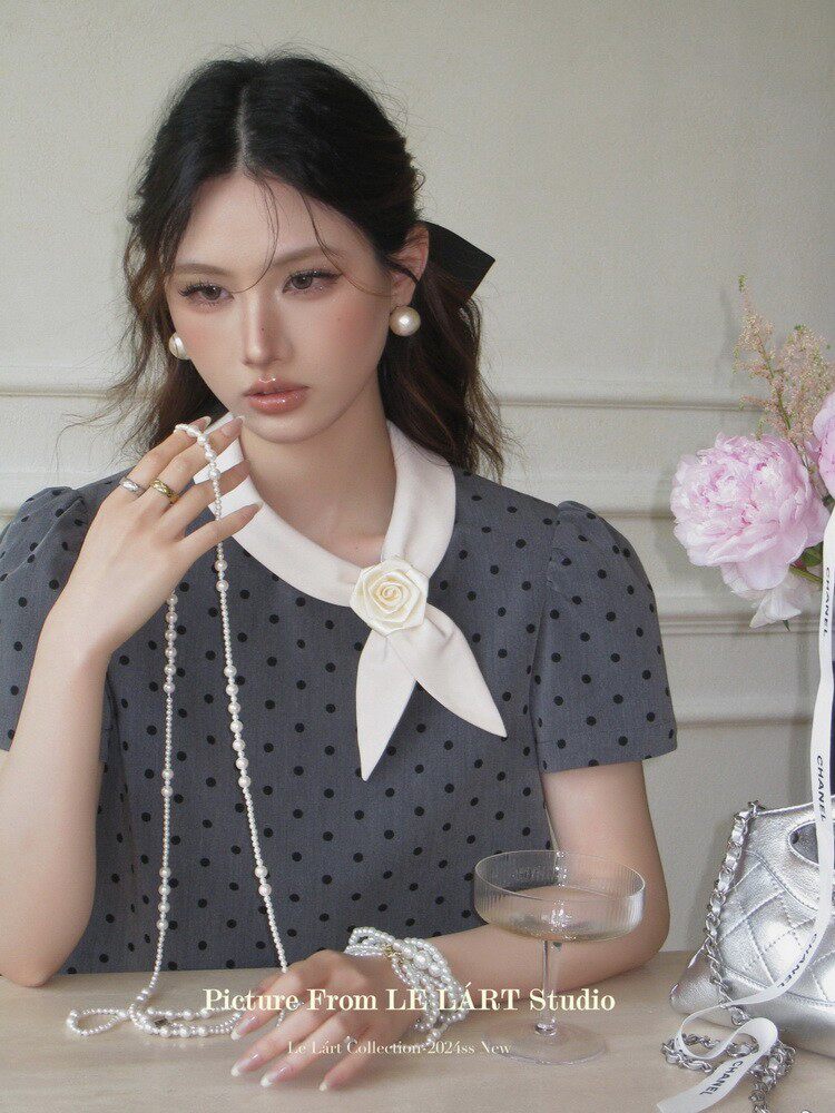 Woman wearing a gray polka dot dress with a white collar and flower detail