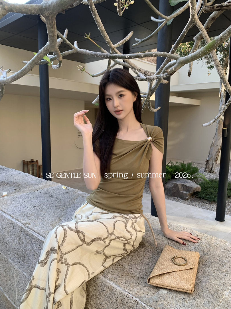 Model wearing an olive draped top with a printed skirt and woven clutch
