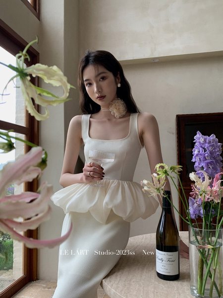 Woman wearing a white sleeveless dress with a floral accent and voluminous peplum detail