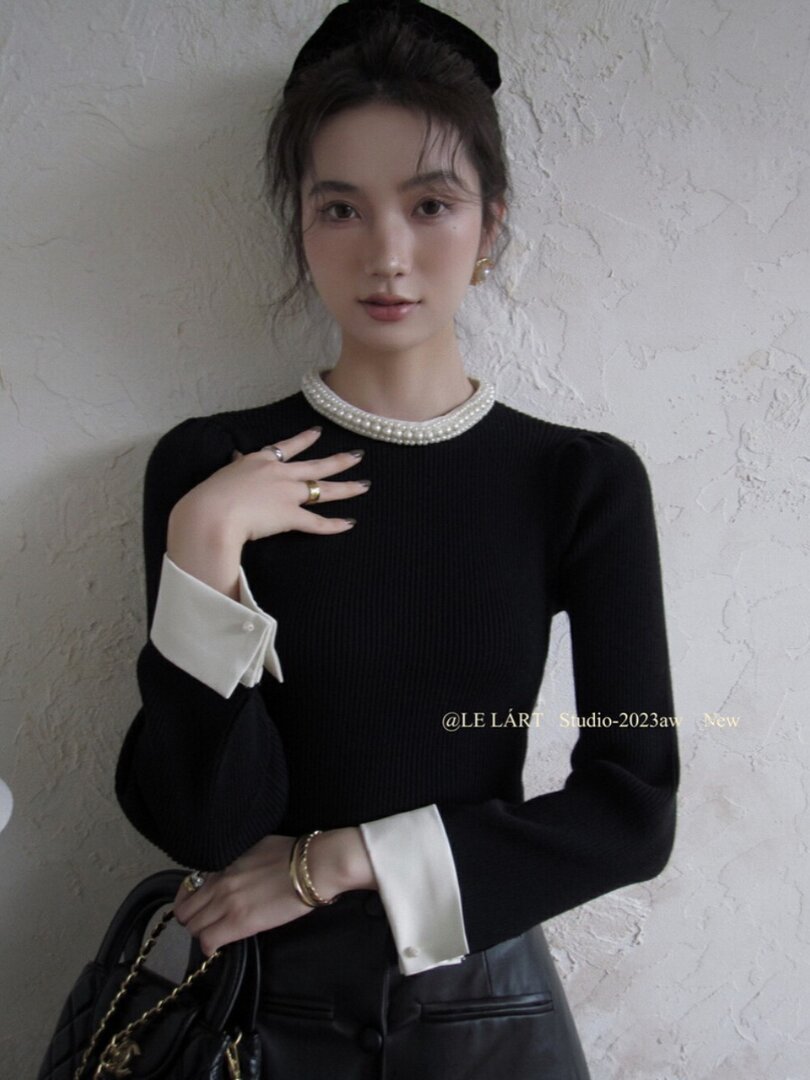 Black long-sleeve top with pearl neckline and white cuffs worn by a model
