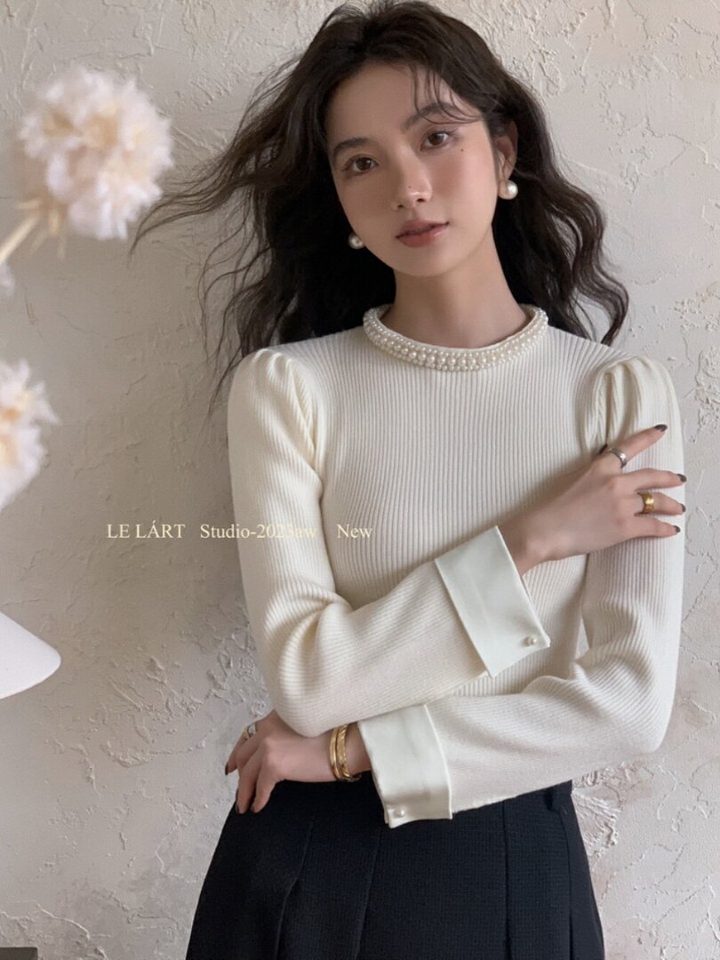 Model wearing a white ribbed long-sleeve top with pearl trim and satin cuffs