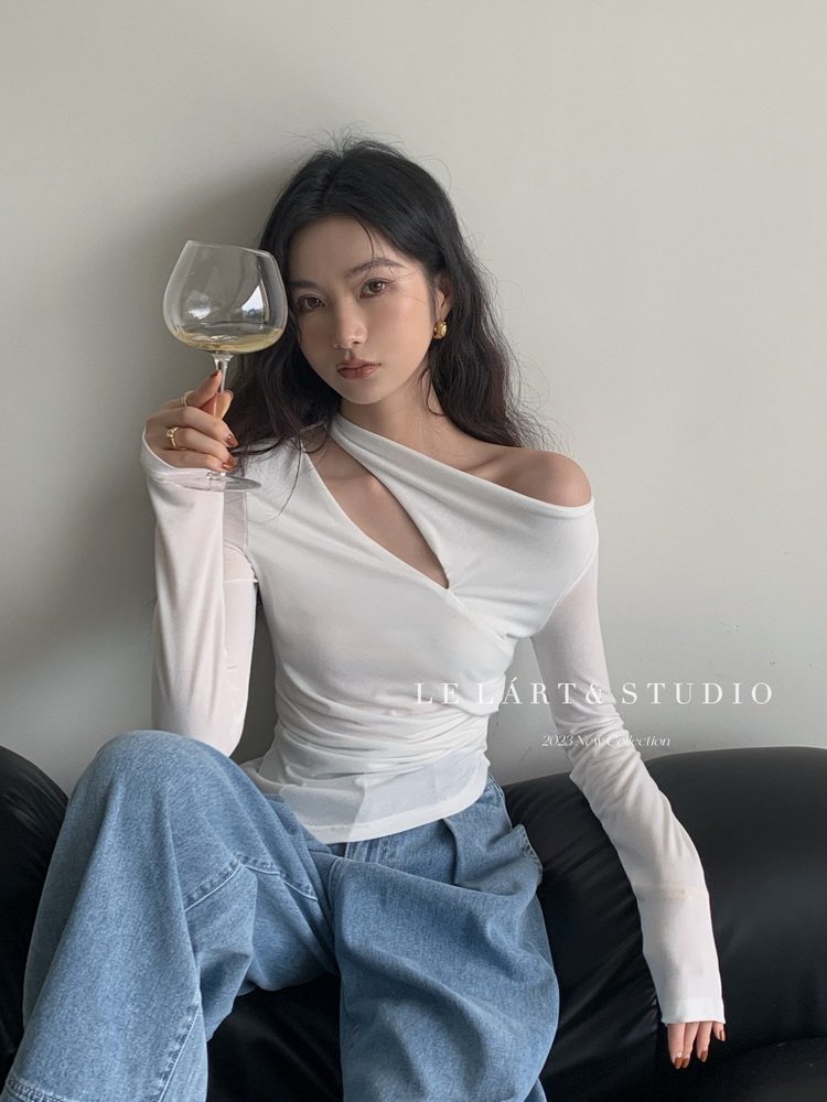 Model wearing a white asymmetrical off-shoulder long-sleeve top with wide blue jeans
