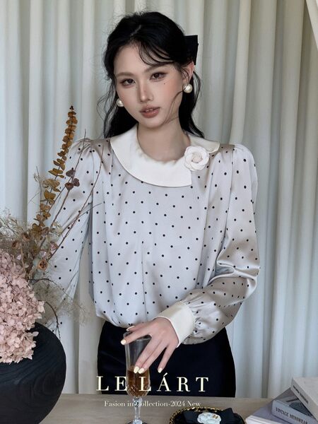 Model wearing a white polka dot blouse with a Peter Pan collar and long sleeves