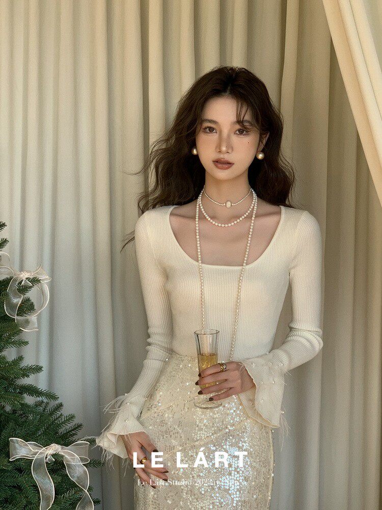 Model wearing a cream fitted long-sleeve top with a sequined skirt and pearl accessories