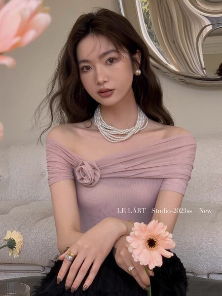Model wearing a pink off-shoulder ruched top with pearl necklace